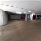 Prázdné parkovací místo v moderní garáži s betonovou podlahou, umělým osvětlením a světlými stěnami.